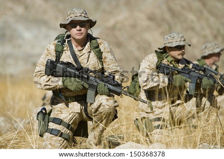 Portrait of confident soldier with rifle while team patrolling in background during war