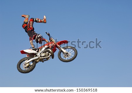 Low angle view of motocross racer performing stunt with motorcycle in midair against clear blue sky