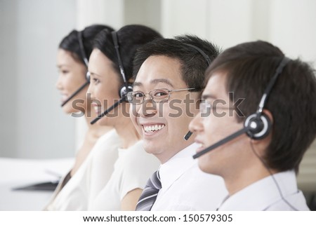 Portrait of young male customer service operator with colleagues working in background