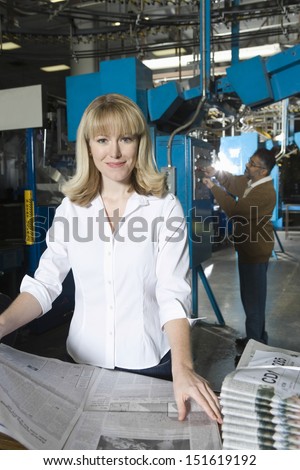 Woman checking newspaper with colleague in the background in factory