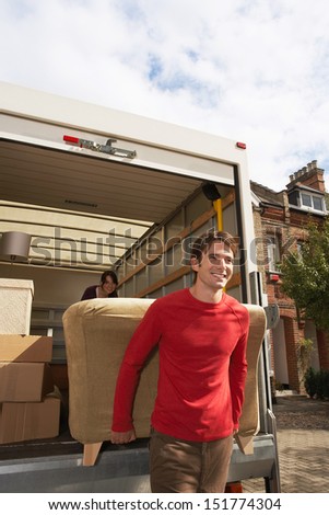 Smiling young couple unloading sofa from truck in front of new house