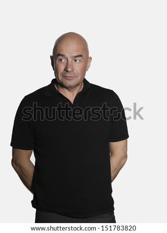 Middle aged man standing with hands behind back and looking sideways on white background