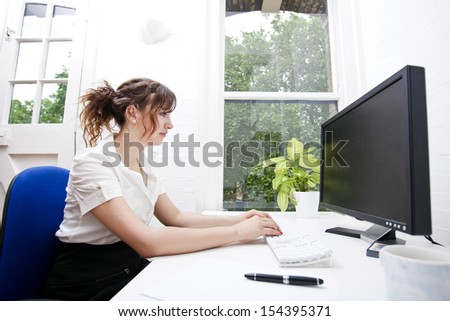 Side view of young businesswoman using computer at desk