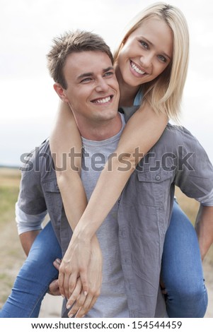Happy young man giving piggyback ride to girlfriend on field