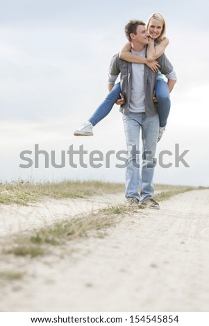 Happy young man giving piggyback ride to woman on trail at field