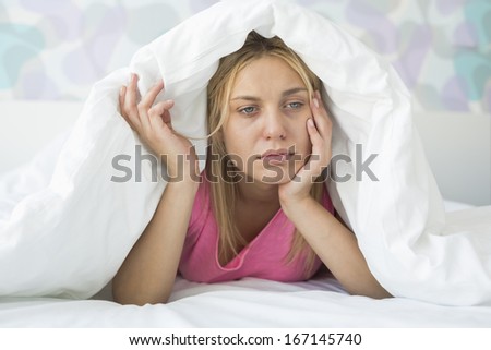 Thoughtful ill woman covered with quilt in bed