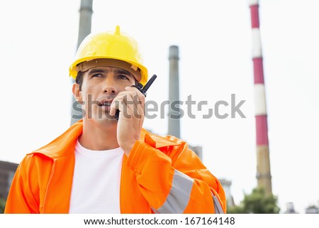 Male construction worker wearing reflective workwear communicating on two way radio at site