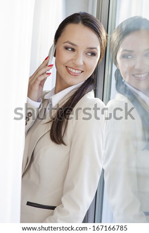 Beautiful businesswoman answering cell phone by window in office