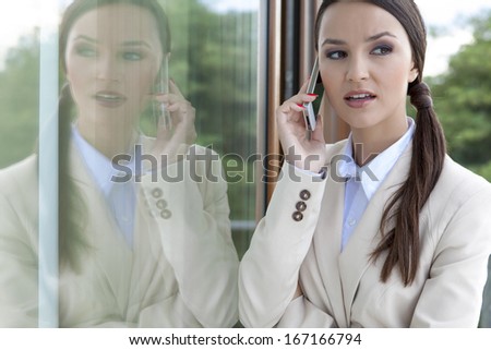 Beautiful businesswoman answering cell phone by glass door