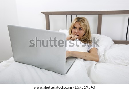 Thoughtful young woman looking at laptop in bed