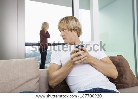 Mid-adult man text messaging while woman using cell phone in background at home