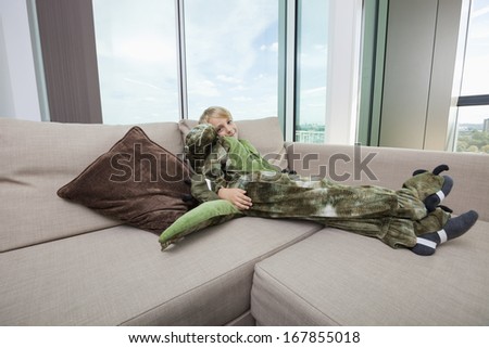 Portrait of boy wearing dinosaur costume relaxing on sofa at home