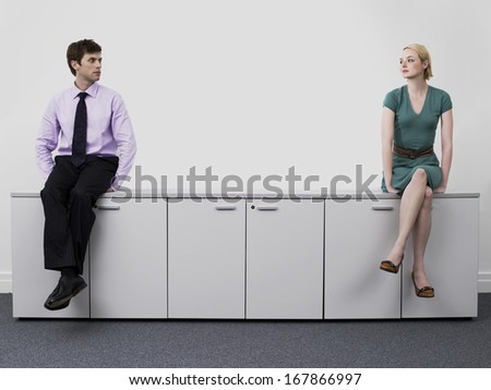 Young male and female business people sitting on office cabinets