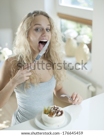 Woman with cake licking table knife at counter in house