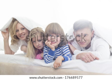Portrait of happy parents and children lying under bed cover