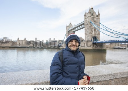 Portrait of mid adult man in warm clothing standing in front of tower bridge; London; UK