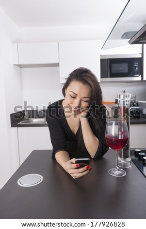 Happy young woman reading text message on smart phone in kitchen