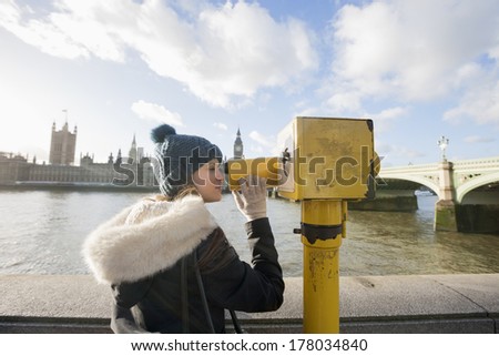 Side view of young woman looking through telescope by river Thames; London; UK