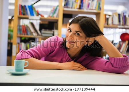 Portrait of young woman with coffee on desk in library