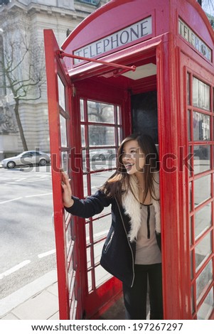 Happy young woman opening door of telephone booth at London; England; UK