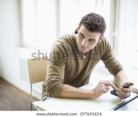 Handsome businessman holding cell phone while looking away in office