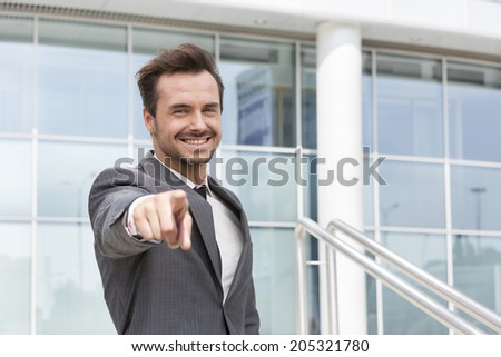 Portrait of happy businessman pointing at you outside office building