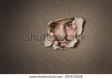 Portrait of a mid adult Caucasian man peeking from ripped paper hole
