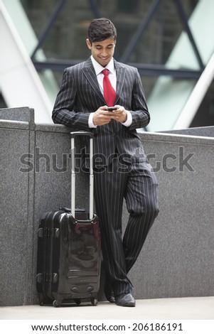 Young Indian businessman with luggage bag using cell phone