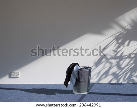 Suit in waste bin on carpeted floor against white wall