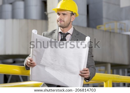 Young businessman holding blueprint while looking away at construction site