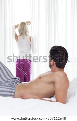Shirtless man looking at woman standing by window in hotel room