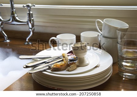 Closeup of a stack of dirty dishes and silverware by sink in the kitchen