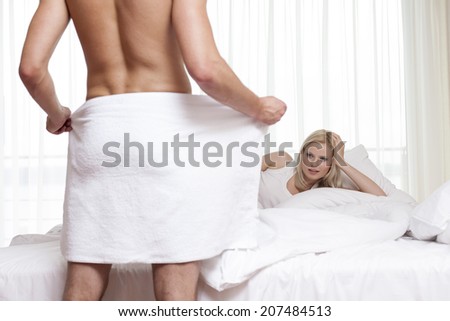 Young man looking at naked man holding towel in bedroom