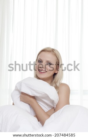 Portrait of attractive young woman covering herself with bedsheet in bed