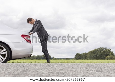 Side view of tired young businessman pushing car at countryside