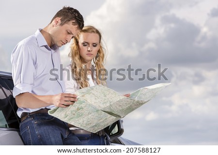 Couple reading map while leaning on car against cloudy sky