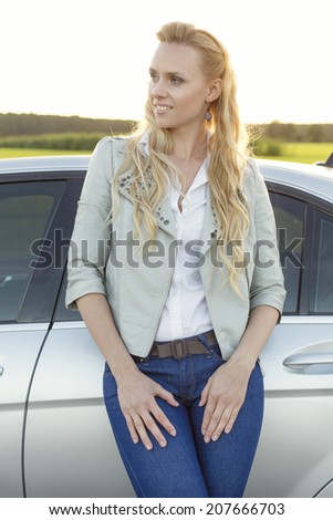 Beautiful young woman looking away while standing by car at countryside