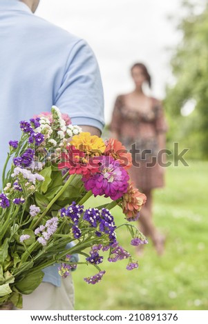 Cropped image of man hiding bouquet from woman in park