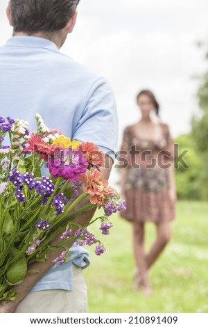 Cropped image of man surprising woman with bouquet in park