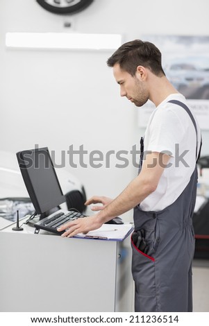 Side view of automobile mechanic using computer in workshop