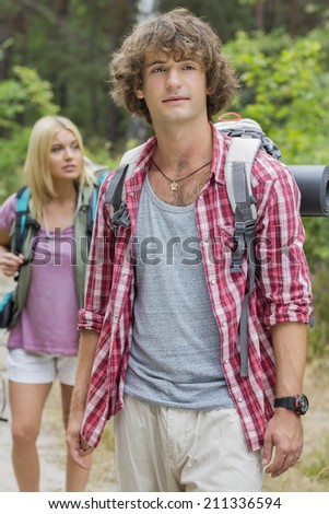 Male backpacker looking away with woman standing in background at forest