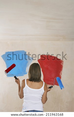 Rear view of a woman painting wall red and blue with paint rollers