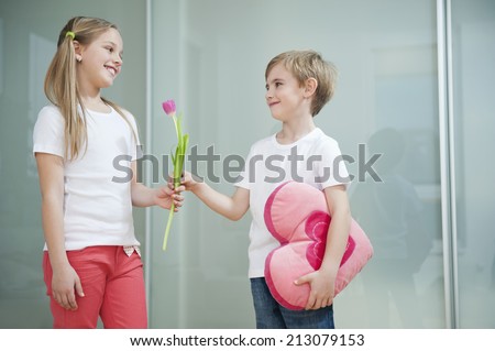 Little boy with heart shape cushion giving flower to girl