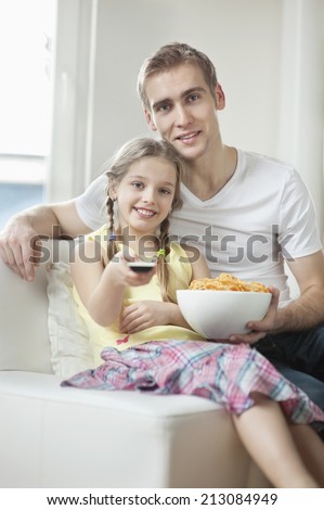 Portrait of father and daughter watching TV with bowl full of wheel shape snack pellets