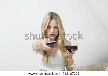Portrait of a young woman holding wine glass while using remote control