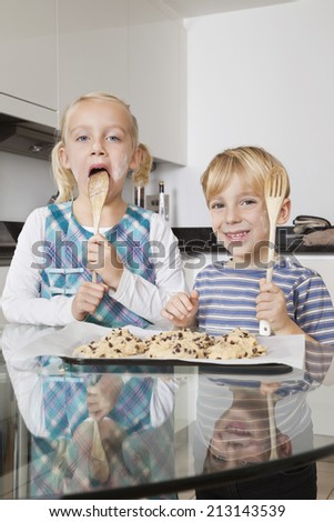 Portrait of happy boy with sister tasting spatula mix with cookie batter in kitchen