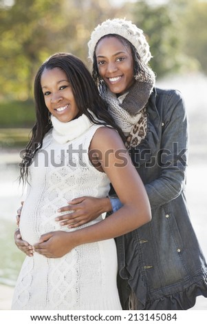Portrait of happy young female friend embracing pregnant woman from behind