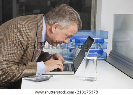 Side view of middle-aged businessman using laptop at desk in office