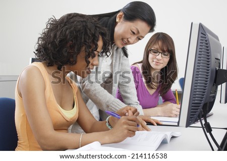 Two female students working with teacher in computer classroom