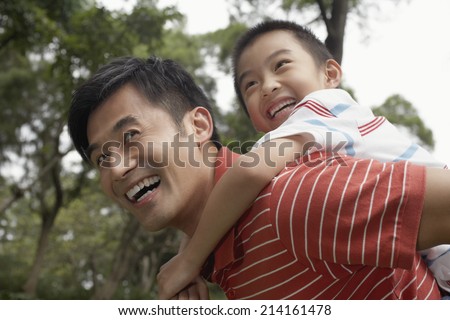 Father giving son piggyback (7-9) in park